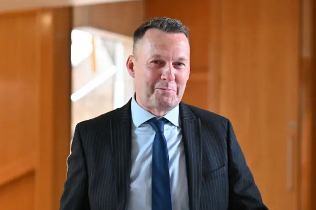 Russell Findlay in a dark suit and tie smiles as he poses for a picture inside Holyrood