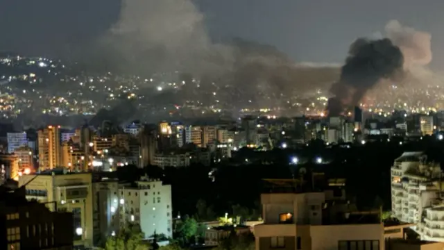 An image showing a city at night with smoke rising in several places above it