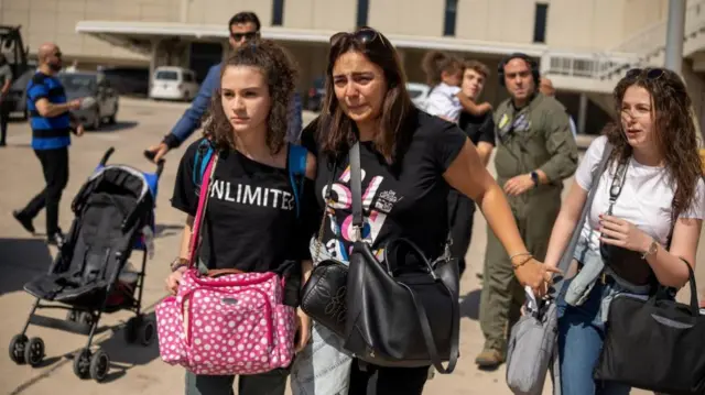 A woman and an two teenage girls look emotional as they walk on the tarmac