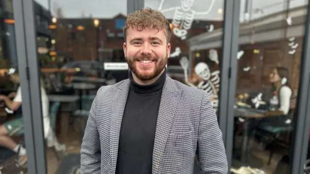 Small business owner Adam stands in front of a window with skeleton decals on it.