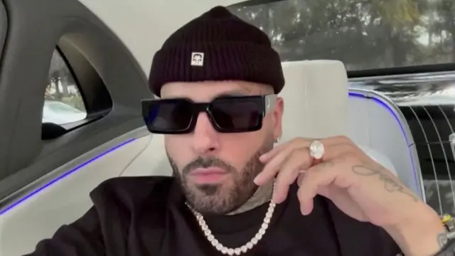 Nicky Jam sits in a car with dark sunglasses on