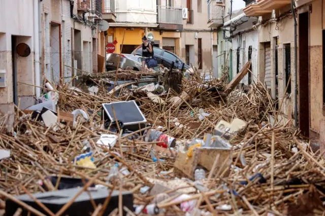 A woman climbs over debris that fills an alleyway.