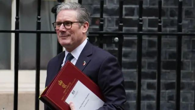 Keir Starmer walking out of 10 Downing St holding a big red folder with Prime Ministers Questions written on the front on white paper