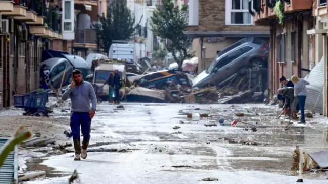 Residents are pictured next to cars piled in a street covered in mud following floods in Picanya, near Valencia, eastern Spain