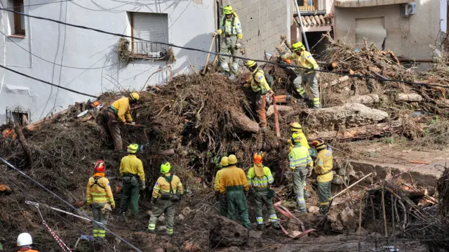 A number of rescue workers, wearing yellow hard hats and fluorescent jackets, search for missing people among a mound of mud and rubble