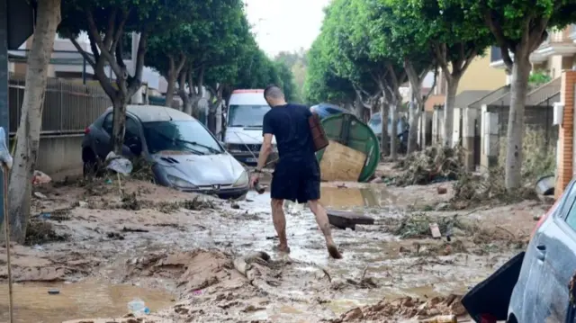 A man walks in a street covered in mud in a flooded area in Picanya