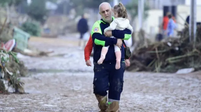 A Civil Protection member carries a child in a street covered in mud in a flooded area in Picanya, near Valencia