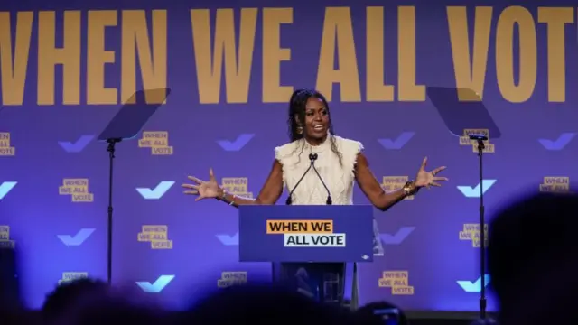 Michelle Obama at a podium reading 'When we all vote' against a purple backdrop with the same logo