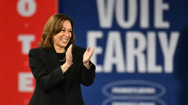 Harris at her rally clapping hands with a sign saying to vote early