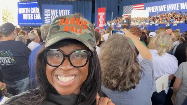 A woman in a Harris Walz hat at a rally event surrounded by people