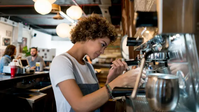 Barista working at a cafe serving a cup of coffee from the machin