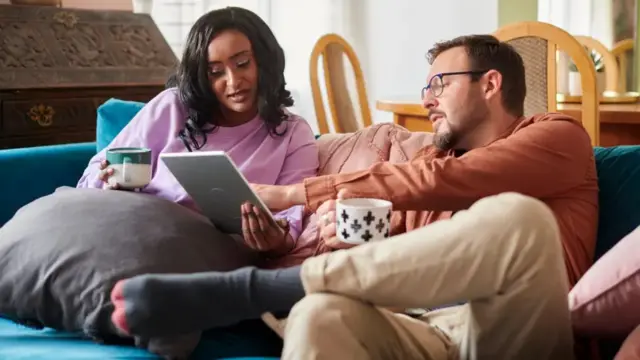 A man and a woman seated on a couch looking at a a tablet