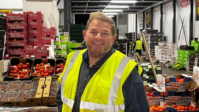 Mark Tate, the director of a fruit and vegetable wholesaler, in front of crates of fruits and vegetables