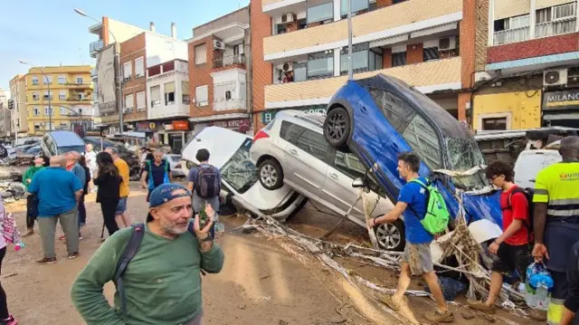 People standing in front of a pile of damaged cars