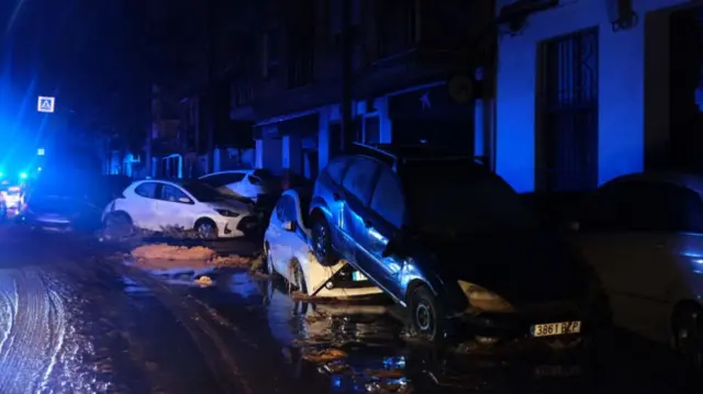 A blue light from an emergency vehicle is seen in the background of cars piled on top of each other