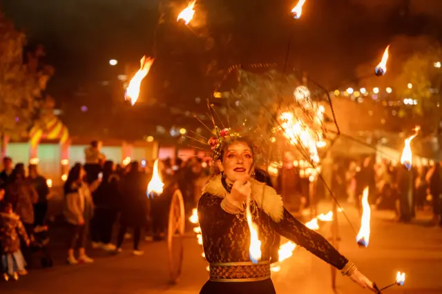 A woman stands in the middle of a crowd, she is juggling fire