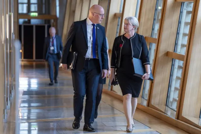 First Minister John Swinney and Finance Minister Shona Robison walk towards Holyrood's chamber.