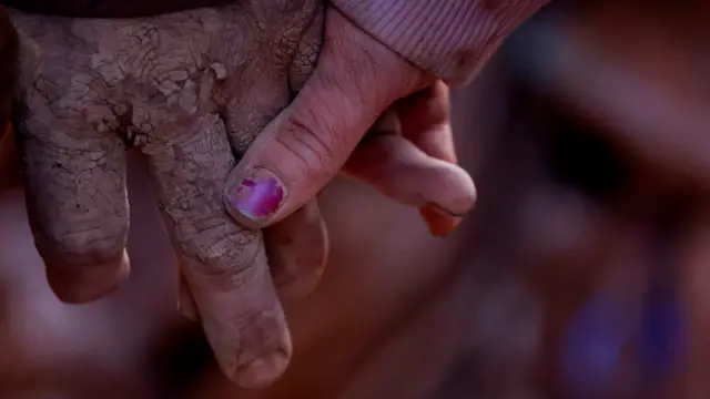 A man and woman, with muddy hands, hold hands