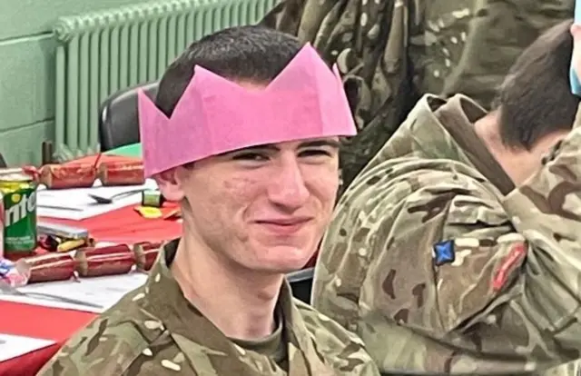 Logan MacPhail in army uniform smiles at the camera, he is wearing a pink hat from a Christmas cracker