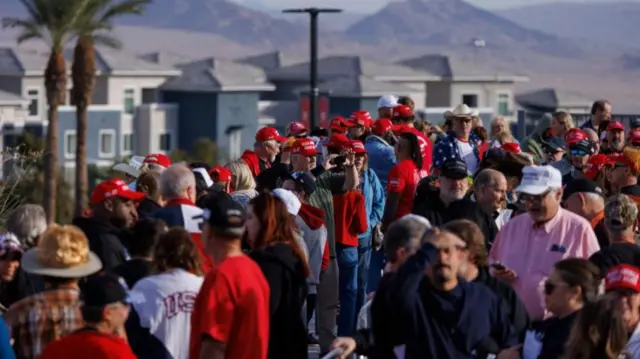 Lines and lines of people, many in MAGA hats, waiting to see Donald Trump. The scenery behind them is mountainous