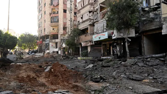 The remains of shops and residential buildings can be seen as rubble lines the main street