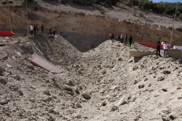 People stand either side of a huge crater at the Masnaa border crossing