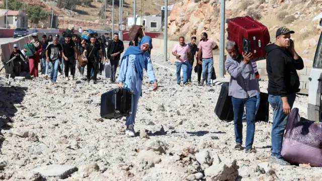 Displaced Lebanese citizens carry luggage across rubble on the Masnaa border with Syria