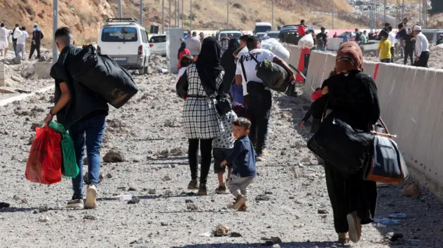 Families carry belongings in bags and suitcases across the Masnaa crossing into Syria, which is littered with rubble after an Israeli striike