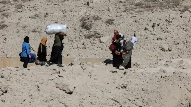 People carrying bags while walking through rubble and rocks