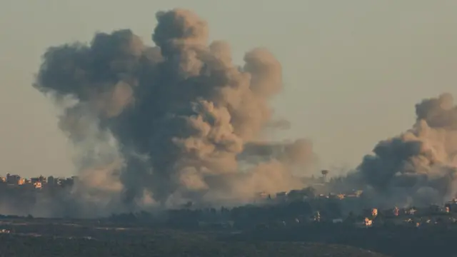 A huge plume of smoke over Tyre, southern Lebanon. Several houses can be seen underneath two huge smoke plumes. The sky is a dark colour, but the sun appears to be out.