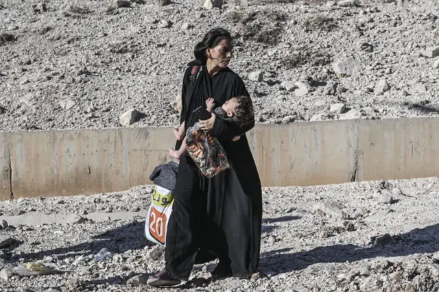 A woman carrying a baby and bags