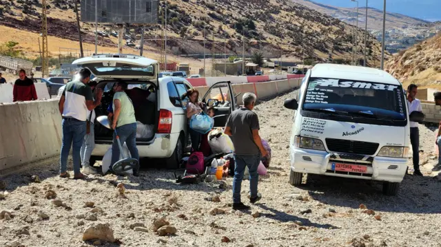 People pull belongings out of vans on the Masnaa crossing into Syria