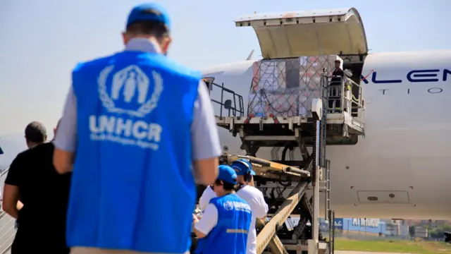 People wearing blue tops with UNHRC written on them stand watching as the plane is unloaded