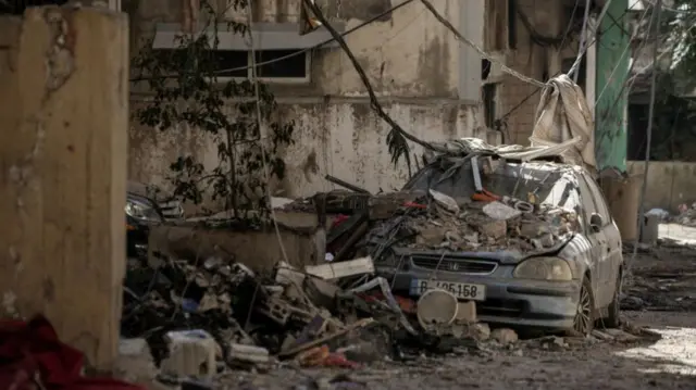 A damaged vehicle lies amidst the rubble in the aftermath of the Israeli strikes