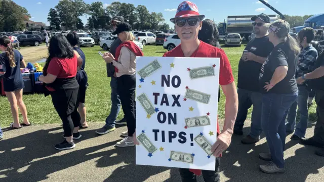 Gino Chiodo speaks to the BBC wearing a board that read "no tax on tips" with dollar bills