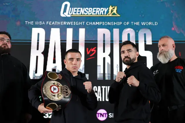 Nick Ball is holding the WBA featherweight title over his shoulder and is standing next to Ronny Rios, who is holding up is fists