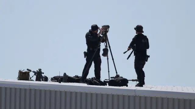 Snipers, with guns at their side, scan crowds using binoculars