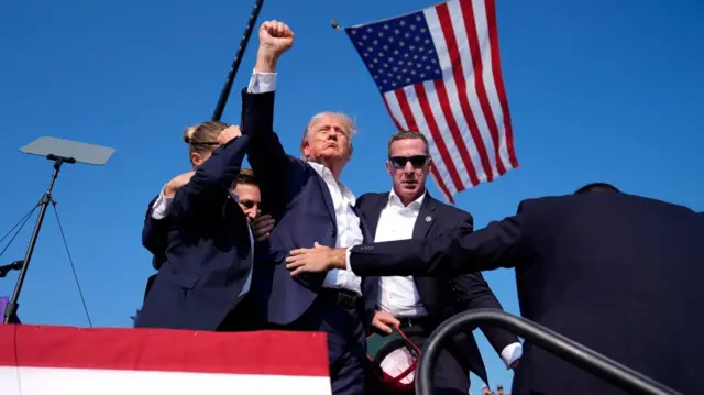 File photo from July shows Republican presidential nominee raising his fist in the air, blood on his face, as he is surrounded by Secret Service agents at a Butler rally