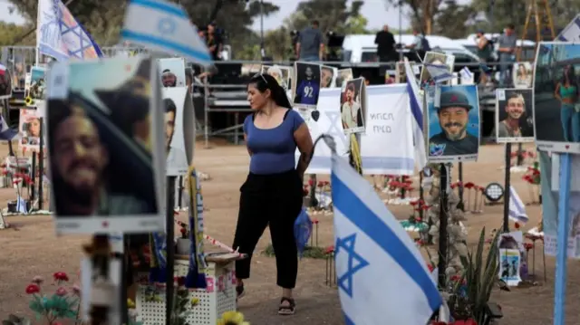 A woman stands among photo tributes and flowers at the site of the Nova festival