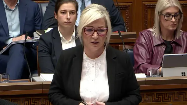 A women with red glasses, white shirt and black blazer