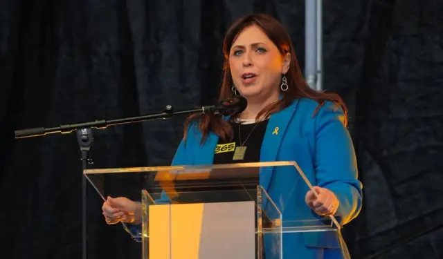 Hotovely delivering speach at lectern wearing blue suit jacked and black shirt