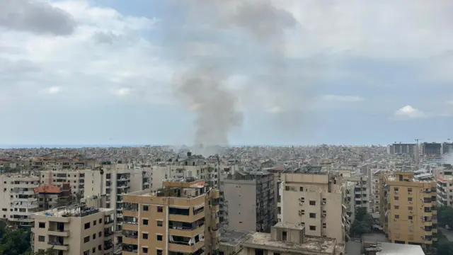 Wide view of apartment rooftops in Dahieh, southern Beirut with plumes of smoke coming out from the middle section