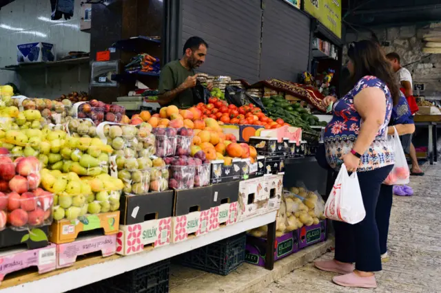 A woman buying fruit at a market stall in the old city in Jerusalem, 9 August 2024