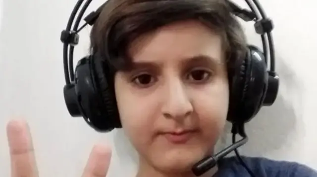 A boy wears headphones and makes a peace sign to the camera