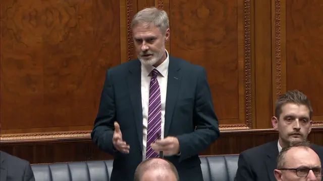 Paul Frew wearing a navy suit, white shirt and pink striped tie