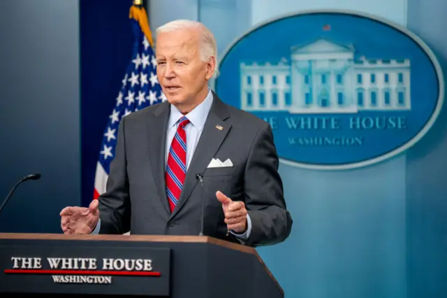 Joe Biden delivers speech in white house wearing dark grey suit and striped red-and-blue tie