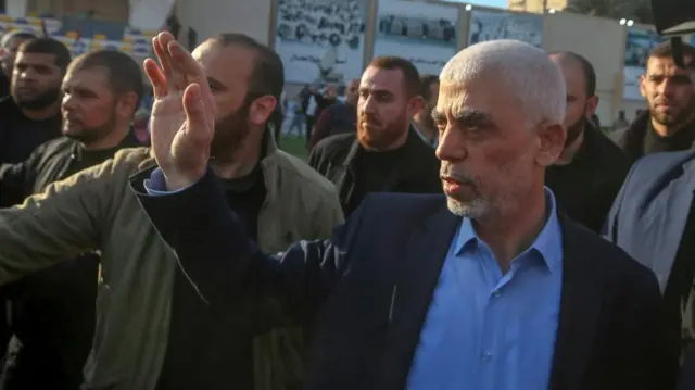 Hamas leader Yahya Sinwar at a rally in Gaza in April 2023, pictured wearing a suit and waving his hand with a group of people behind him