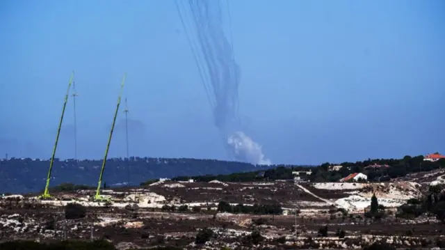 Rockets are launched from Lebanon towards Israel, there is smoke in the air over rolling hills and trees