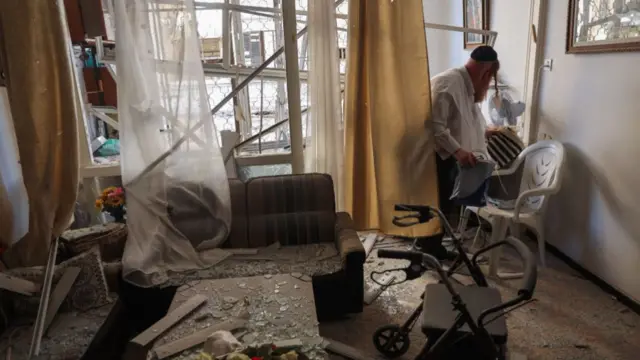 A man inspects a damaged apartment in a building which was hit with a rocket launched from Lebanon