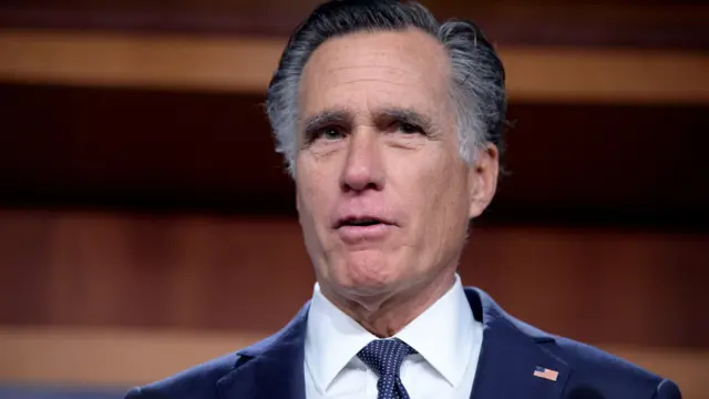 Utah Senator Mitt Romney, wearing a blue suit and shite shirt, pulls a facial expression